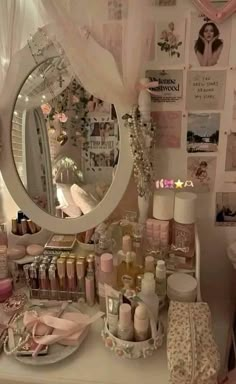 a white vanity topped with lots of cosmetics and bottles next to a round shaped mirror