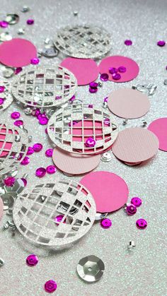 some pink and silver confetti on a table with other confetti pieces