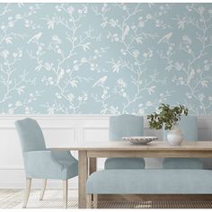 a dining room table with blue chairs and a wallpapered background that has white flowers on it