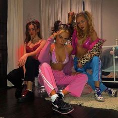 three women in pink outfits are sitting on the floor and one woman is holding up her hair