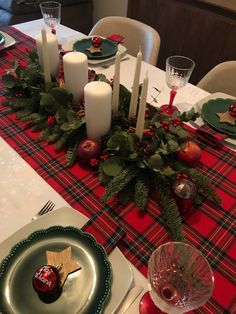 the table is set for christmas dinner with candles, apples and greenery on it