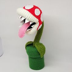 a crocheted mushroom with its mouth open and tongue out, sitting on top of a green cup