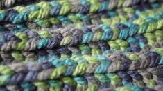 a close up view of a crocheted blanket with green, blue and grey colors