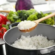 a person spooning rice out of a pot with vegetables in the backgroud