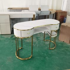 two white desks with gold trim on them in a room filled with boxes and other furniture