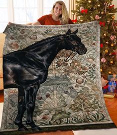 a woman holding up a black horse on a christmas blanket in front of a tree