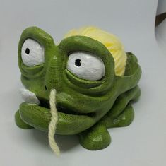 an odd looking green toy with eyes and a ball of yarn in it's mouth