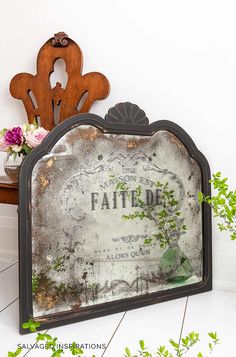 an old mirror is sitting on the floor next to a table with flowers in it