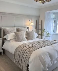 a bed with white linens and pillows in a bedroom next to a large window