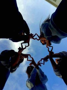 four people are standing in a circle holding their hands up to the sky and making a heart shape