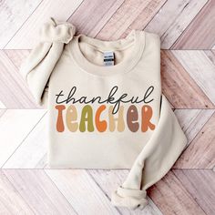 Thankful Teacher Sweatshirt, Thanksgiving Teacher Shirts for Men & Women, Thanksgiving Gift for Teacher, Autumn Teacher Tees, Fall Vibes Tee ---------- Ordering Your Custom Design T-shirt: Step by Step ---------- 1. Select your preferred t-shirt color. 2. Specify your desired size. 3. Pick the color for both your design and text. 4. Ensure that each step of your order is accurately completed. M A T E R I A L S → Our solid color options such as White and Black consist of 100% Cotton. → The Heathered Colors are a blend of cotton and polyester, ensuring a luxuriously soft feel. → Crafted as Short Sleeve Crew-Neck Unisex T-Shirts. → Composed of soft, high-quality Sueded Jersey fabric. → Taped shoulder-to-shoulder for enhanced durability. → Side Seamed for a refined finish. → Boasts a Retail fi Fall Teacher Shirt, Long Sleeve Cotton T-shirt With Lettering, Fall Text Print Short Sleeve Sweatshirt, Fall Short Sleeve Sweatshirt With Text Print, Short Sleeve Sweatshirt With Text Print For Fall, Fall Cotton Tops With Lettering, Thanksgiving Teacher Shirts, Fall Teacher Shirts, Teacher Sweatshirt