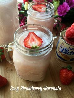 two mason jars filled with strawberry milk and topped with fresh strawberries next to pink flowers