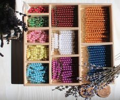 an open wooden box filled with lots of different colored beads next to a vase and dried flowers