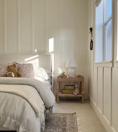 a teddy bear sitting on top of a bed next to a night stand and window