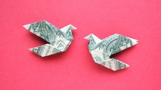 two origami birds made out of dollar bills on a pink background, one is folded in half