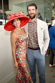 a man and woman standing next to each other in front of a wall wearing hats