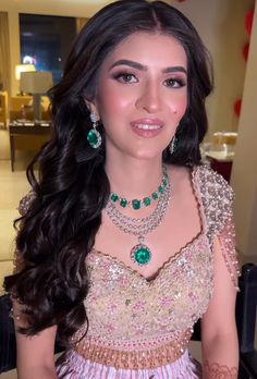 a woman in a pink dress with green jewelry on her neck and shoulder, smiling at the camera