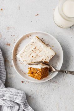 a white plate topped with a piece of cake next to a cup of milk and a spoon