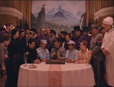 a group of people sitting around a table in front of a painting on the wall