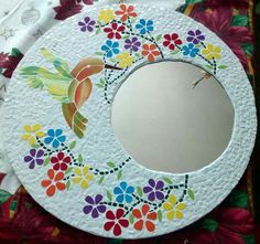 a white plate with colorful flowers painted on it and a mirror hanging from the side