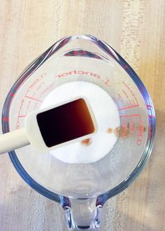 a blender filled with brown liquid on top of a wooden table next to a measuring cup