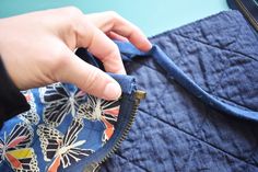 a hand is opening the zipper on a blue quilted piece of cloth that has butterfly designs