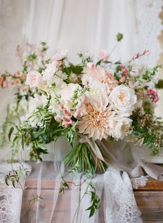 a vase filled with lots of flowers on top of a wooden table covered in lace