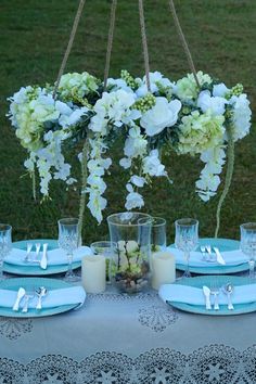 the table is set with white flowers and blue place settings for two people to eat