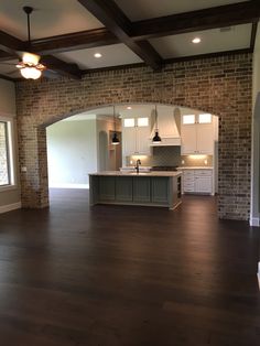 an empty kitchen and living room in a house with wood floors, exposed beams, and brick walls