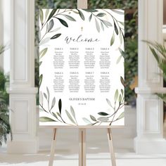 an easel with a wedding seating chart on it and greenery in the background