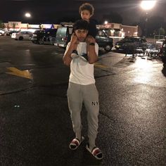 a man holding a young boy on his shoulders in the middle of a parking lot