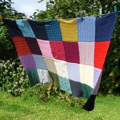 a multicolored quilt hanging on a clothes line in the grass next to flowers