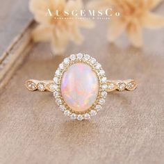 an opal and diamond ring on a wooden surface with flowers in the back ground