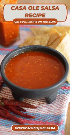 a bowl of red sauce sitting on top of a table next to tortilla chips