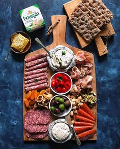 an assortment of meats and cheeses on a cutting board next to crackers