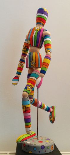 a multicolored wooden figure standing on top of a black table next to a white wall