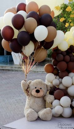 a teddy bear holding balloons in front of a bunch of other balloons on the ground