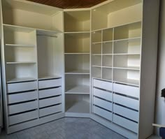 an empty walk in closet with lots of white drawers and shelving unit doors open