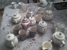 a table topped with lots of white cups and saucers on top of a lace covered table cloth