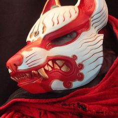 a red and white mask with an animal's face painted on it, sitting on top of a black cloth