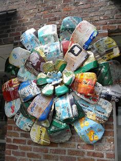 a circular sculpture made out of beer cans on the side of a building with a brick wall behind it