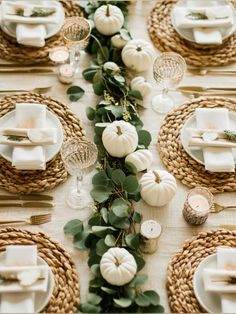 the table is set with white pumpkins, greenery and place settings for dinner