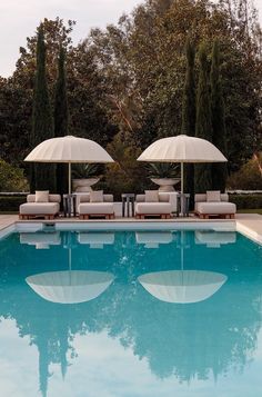 two lounge chairs with umbrellas next to a swimming pool