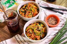 two bowls filled with noodles and vegetables on top of a table next to chopsticks