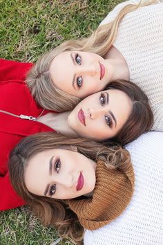 three women are laying on the grass and posing for a photo with their heads together