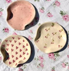 three bowls with hearts painted on them are sitting on a tablecloth, one is empty and the other has pink flowers