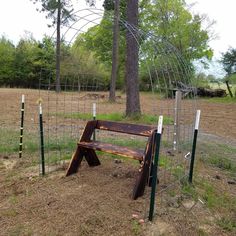 a wooden bench sitting in the middle of a field next to a wire fence and trees