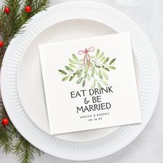 a white plate topped with a card next to a pine branch and red berries on top of it