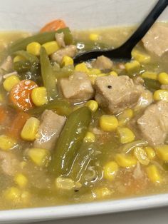 a white bowl filled with corn and meat soup next to a black spoon on top of a table