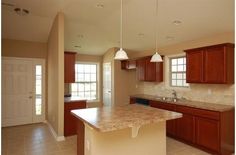 an empty kitchen with marble counter tops and wooden cabinets, along with tile flooring